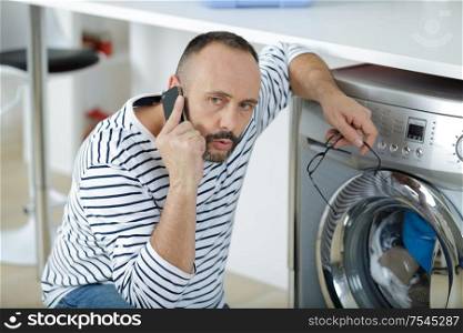 man on telephone kneeling by washing machine