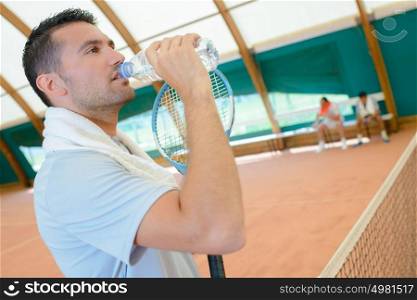 Man on tennis court drinking from water bottle