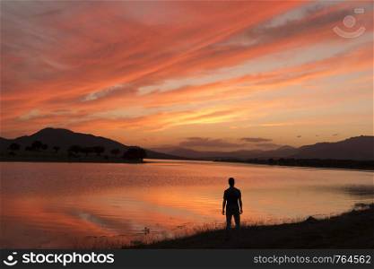 Man on the lake shore contemplates an amazing sunset