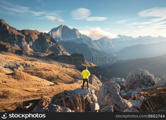Man on the mountain peak and beautiful high rocks at colorful sunset in autumn in Dolomites, Italy. Landscape with sporty guy on the stone, cliffs, grass, blue sky in fall. Trekking and hiking	