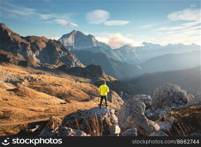 Man on the mountain peak and beautiful high rocks at colorful sunset in autumn in Dolomites, Italy. Landscape with sporty guy on the stone, cliffs, grass, blue sky in fall. Trekking and hiking	