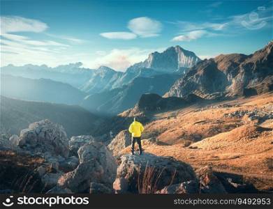 Man on the mountain peak and beautiful high rocks at colorful sunset in autumn in Dolomites, Italy. Landscape with sporty guy on the stone, cliffs, orange grass, blue sky in fall. Trekking and hiking 