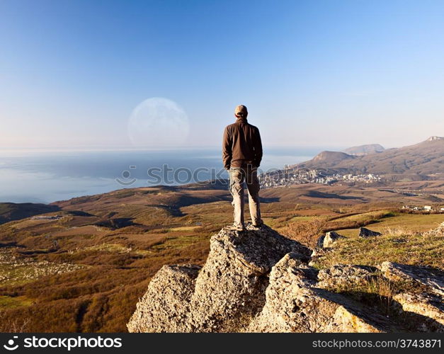 Man on the top of the mountain looking at full moon