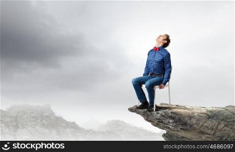 Man on top. Emotional businessman sitting in chair on top of mountain