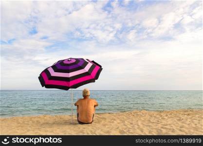 man on vacation with shade under umbrella at the beach