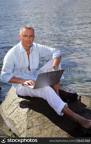 man on vacation working on his laptop near the sea