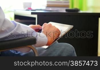 Man on wheelchair working in a home office, using a tablet computer closeup