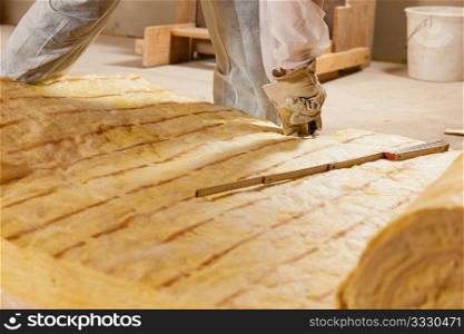 Man - only hand to be seen - cutting some glass wool as material for thermal insulation of a new building