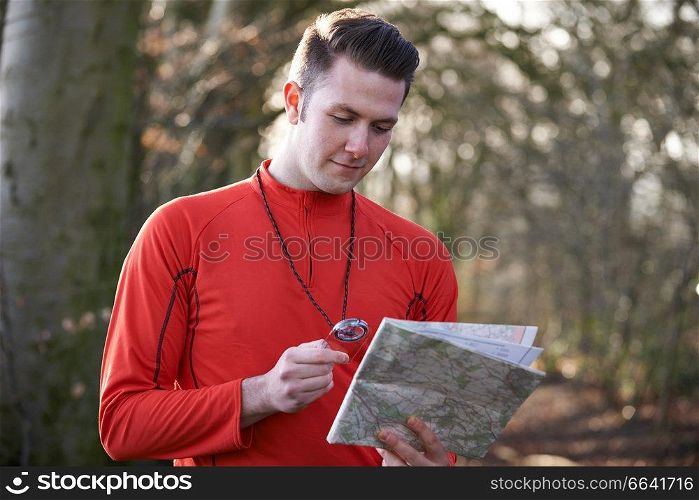 Man Orienteering In Woodlands With Map And Compass
