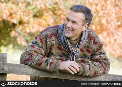 Man outdoors at park leaning on fence smiling (selective focus)