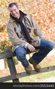 Man outdoors at park sitting on fence smiling (selective focus)