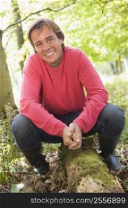 Man outdoors in woods sitting on log smiling