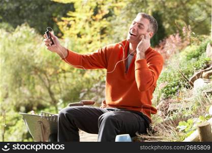 Man Outdoors Listening To MP3 Player Whilst On Break From Gardening