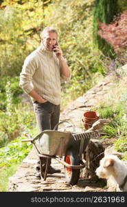 Man Outdoors On Mobile Phone With Dog Whilst On Break From Gardening