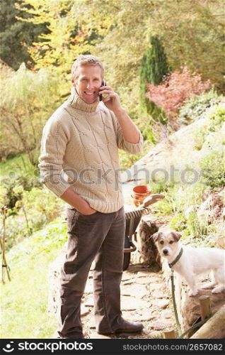 Man Outdoors On Mobile Phone With Dog Whilst On Break From Gardening
