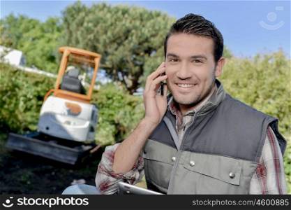 Man outdoors on telephone, digger in background