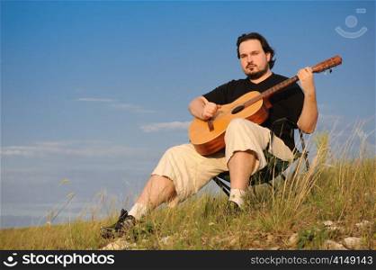 man outdoors playing acoustic guitar, in rays of sunset. guitarist outdoors