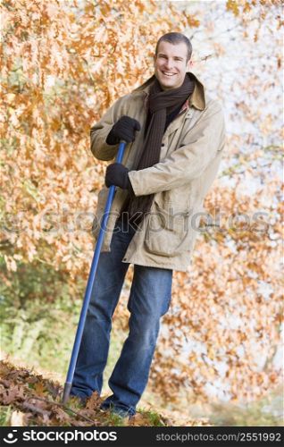 Man outdoors raking leaves and smiling (selective focus)