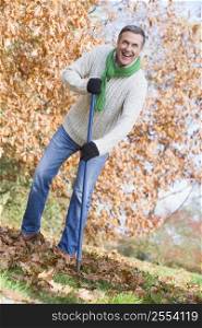 Man outdoors raking leaves and smiling (selective focus)