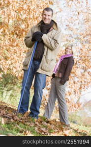 Man outdoors raking leaves and woman in background smiling (selective focus)