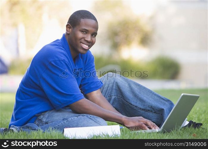 Man outdoors sitting on grass with laptop (selective focus)