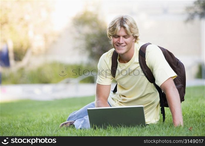 Man outdoors sitting on grass with laptop (selective focus)