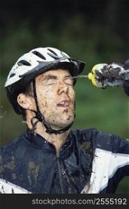 Man outdoors wearing bicycle helmet and splashing water on face (selective focus)