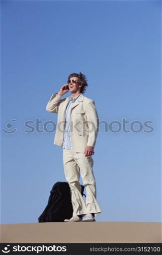 Man outdoors with suitcase using cellular phone