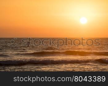 Man paddleboarding in open water at sunset