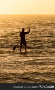 Man paddleboarding in open water at sunset