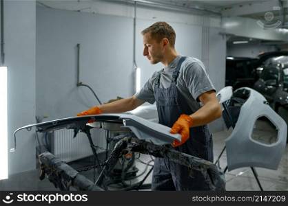 Man painter looking at finished car body segment while working in painting booth. Auto maintenance. Man painter looking at finished car body