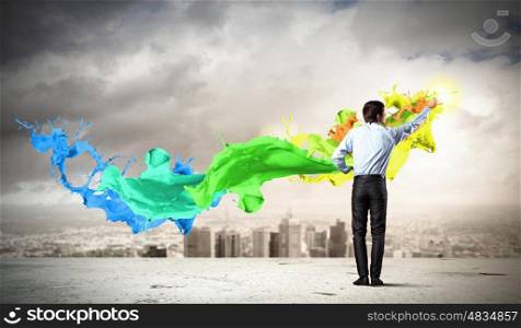 Man painting splashes. young man standing with back painting splashes against city background