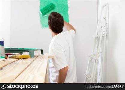 Man painting the wall with roller and brush, stepladder in background