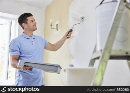 Man Painting Wall In Room Of House With Paint Roller