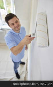 Man Painting Wall In Room Of House With Paint Roller