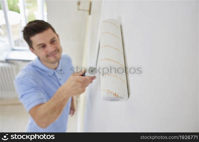 Man Painting Wall In Room Of House With Paint Roller