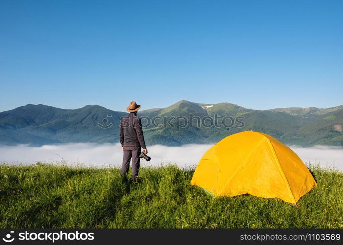 Man photographer with photo camera shooting foggy mountains summer landscape near camping tent. Travel and Lifestyle concept.