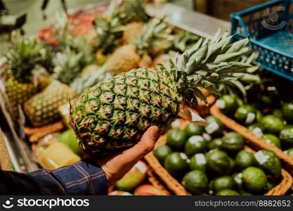 Man picks pineapple - tropical fruit in supermarket or market. sale of healthy and tasty product, vitamins. High quality photo. Man picks pineapple - tropical fruit in supermarket or market. sale of healthy 