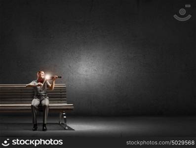 Man play violin. Young handsome man sitting on bench and playing violin