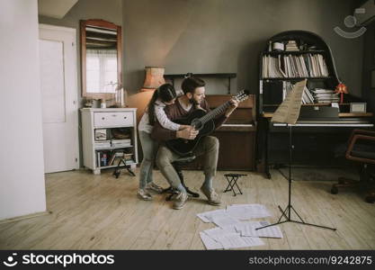 Man playing acoustic guitar for daughter in living room at home