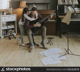 Man playing acoustic guitar for daughter in living room at home