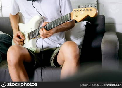 Man playing electrical guitar on sofa at home