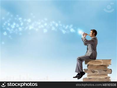 Man playing flute. Young carefree businessman sitting on pile of books and playing on flute