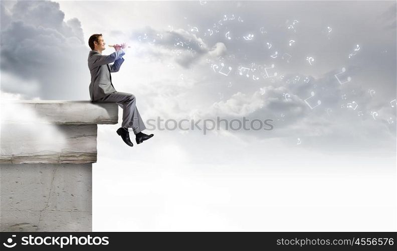 Man playing flute. Young carefree businessman sitting on top of building and playing flute
