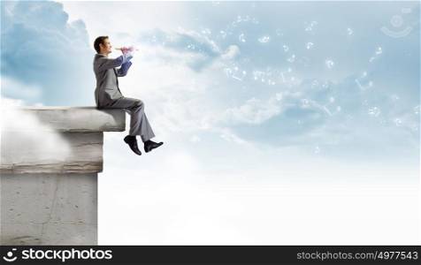 Man playing flute. Young carefree businessman sitting on top of building and playing flute