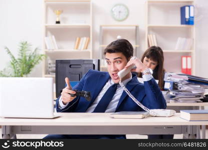 Man playing games in office while colleague is busy