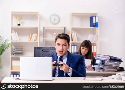 Man playing games in office while colleague is busy