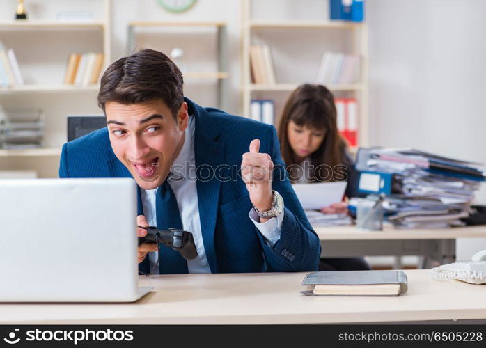 Man playing games in office while colleague is busy