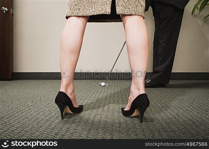 Man playing golf through woman's legs
