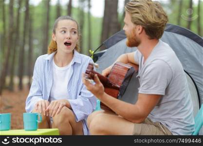 man playing guitar and woman singing by their tent